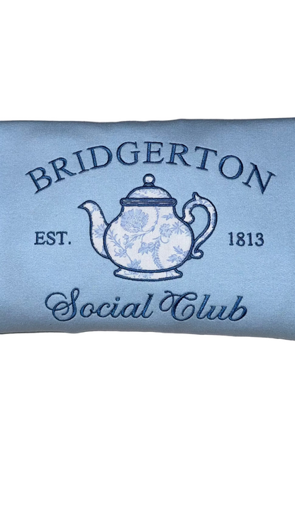 Close up of Bridgerton Social Club sweatshirt design featuring teapot illustration and vintage lettering on light blue crewneck